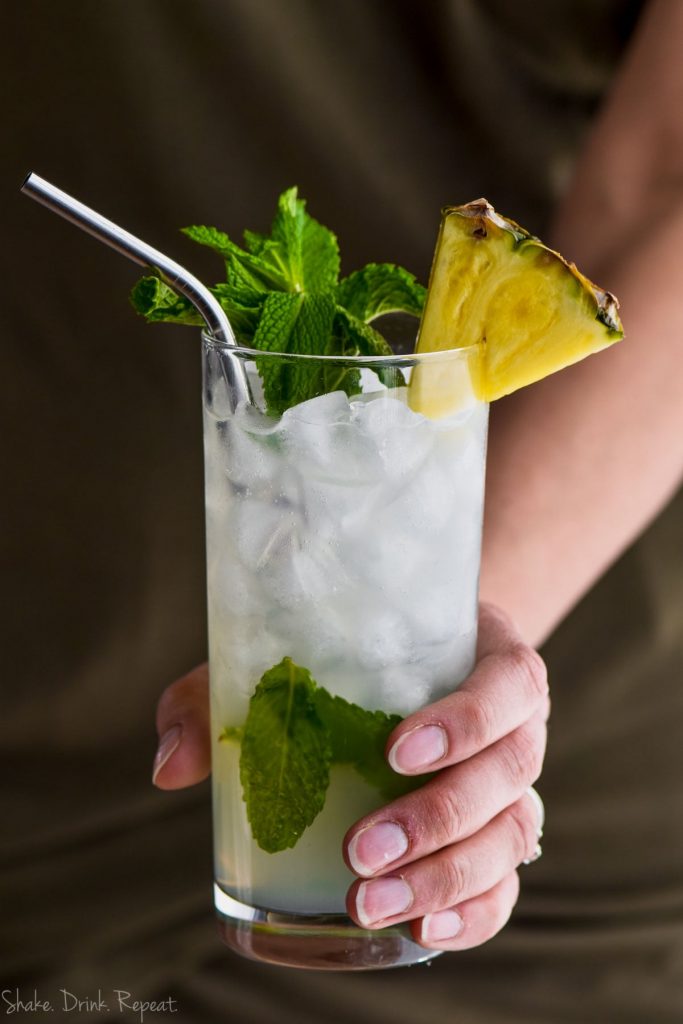 hand holding a pineapple mojito garnished with mint and fresh pineapple 