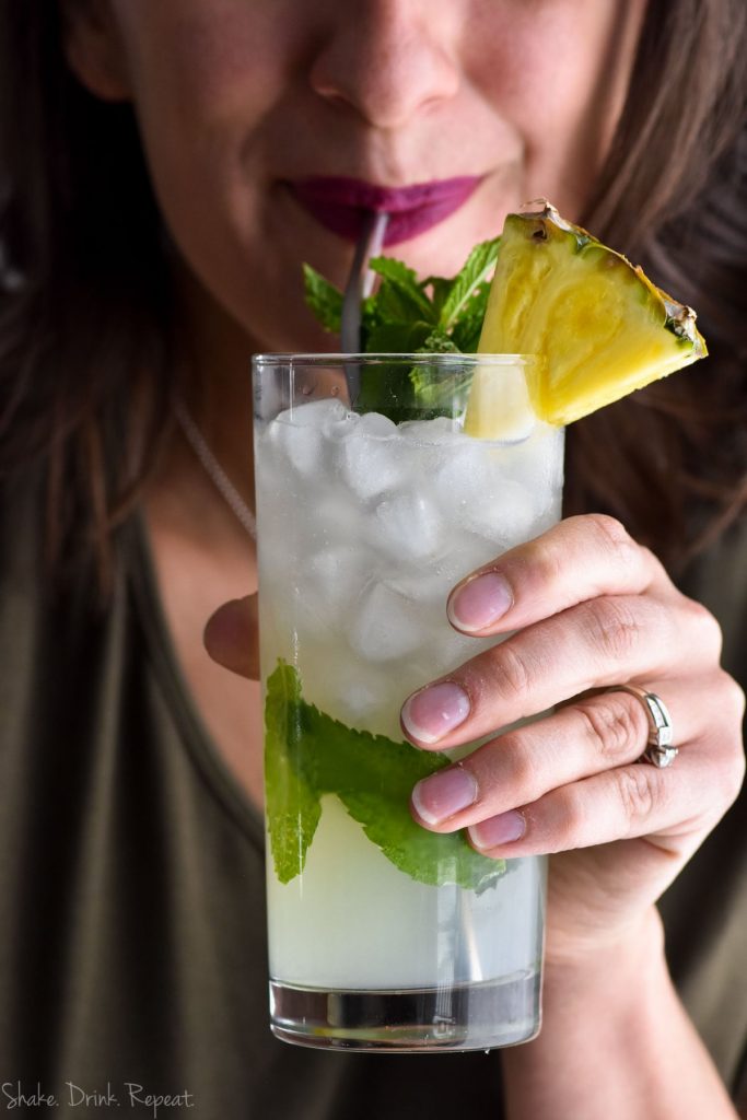 woman sipping pineapple mojito through a metal straw