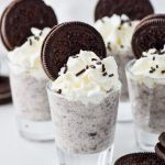 four cookies and cream pudding shots topped with whipped cream and oreos