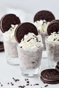 four cookies and cream pudding shots topped with whipped cream and oreos