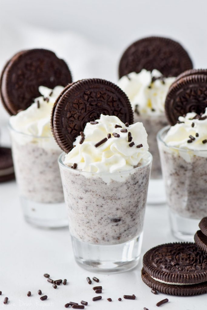 four cookies and cream pudding shots topped with whipped cream and oreos