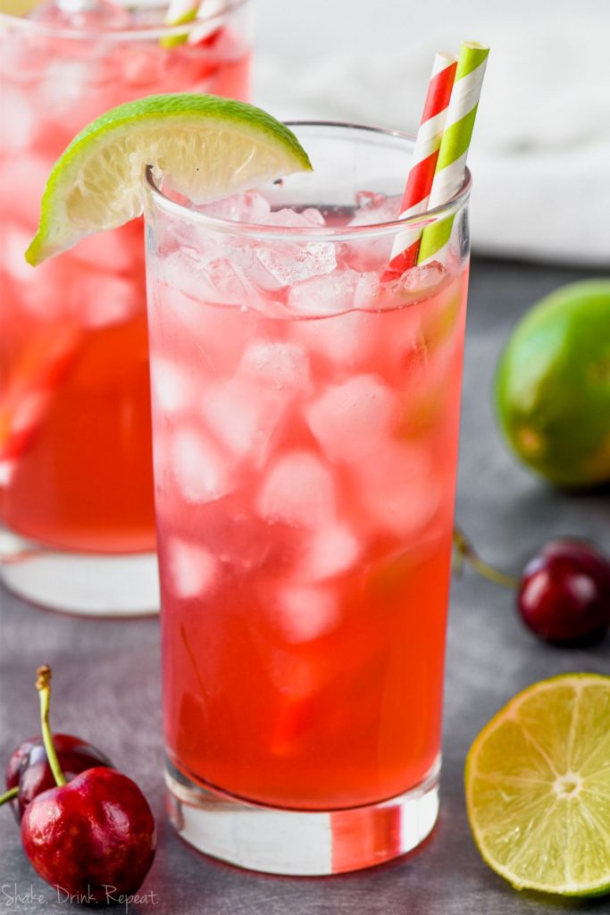 an ice filled glass full of red cherry lime vodka tonics