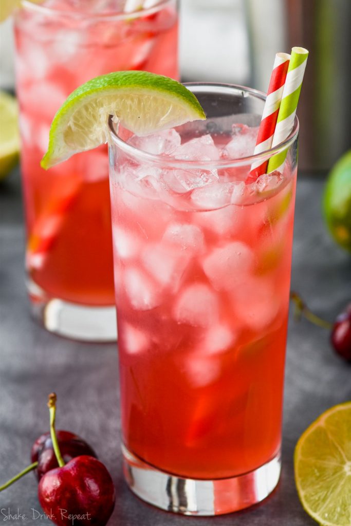 an ice filled glass full of red cherry lime vodka tonics