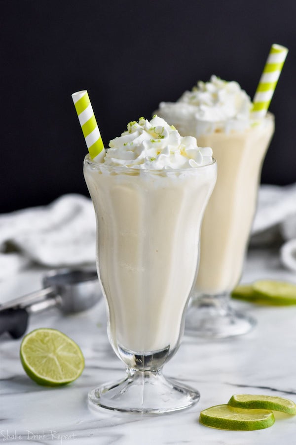 margarita milkshake in a tall milkshake glass with whipped cream and lime zest