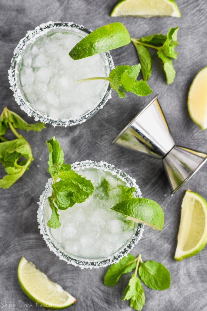 overhead view of two mojito margaritas in salt rimmed glasses with mint and lime wedges