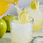 caramel apple vodka punch being poured into a glass of ice garnished with sliced apples