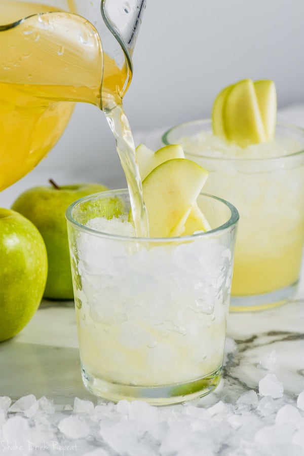 caramel apple vodka punch being poured into a glass of ice garnished with sliced apples