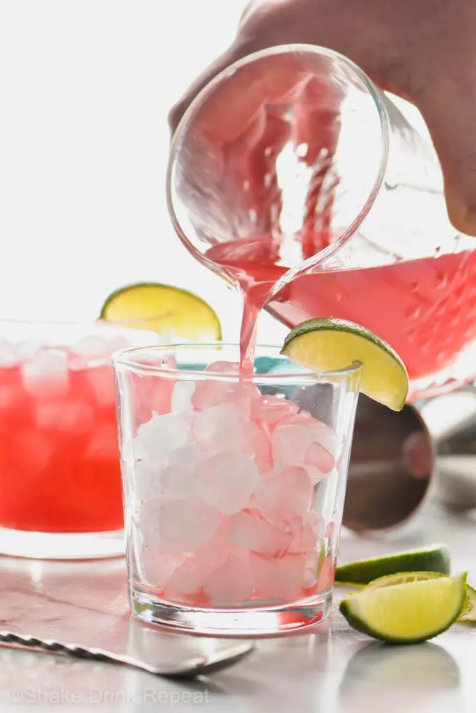 Picture of Sea Breeze being poured into a glass from a pitcher. Drink in a glass garnished with limes