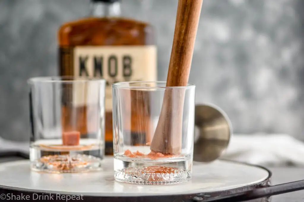 Two glasses with sugar muddled in them with a muddler in one glass