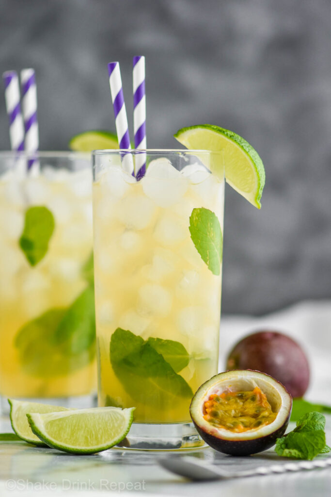 Two glasses of Passion Fruit Mojito with ice, straws, limes, mint and fresh fruit.