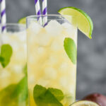 Two glasses of Passion Fruit Mojito with ice, straws, limes, mint and fresh fruit.