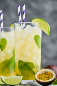 Two glasses of Passion Fruit Mojito with ice, straws, limes, mint and fresh fruit.