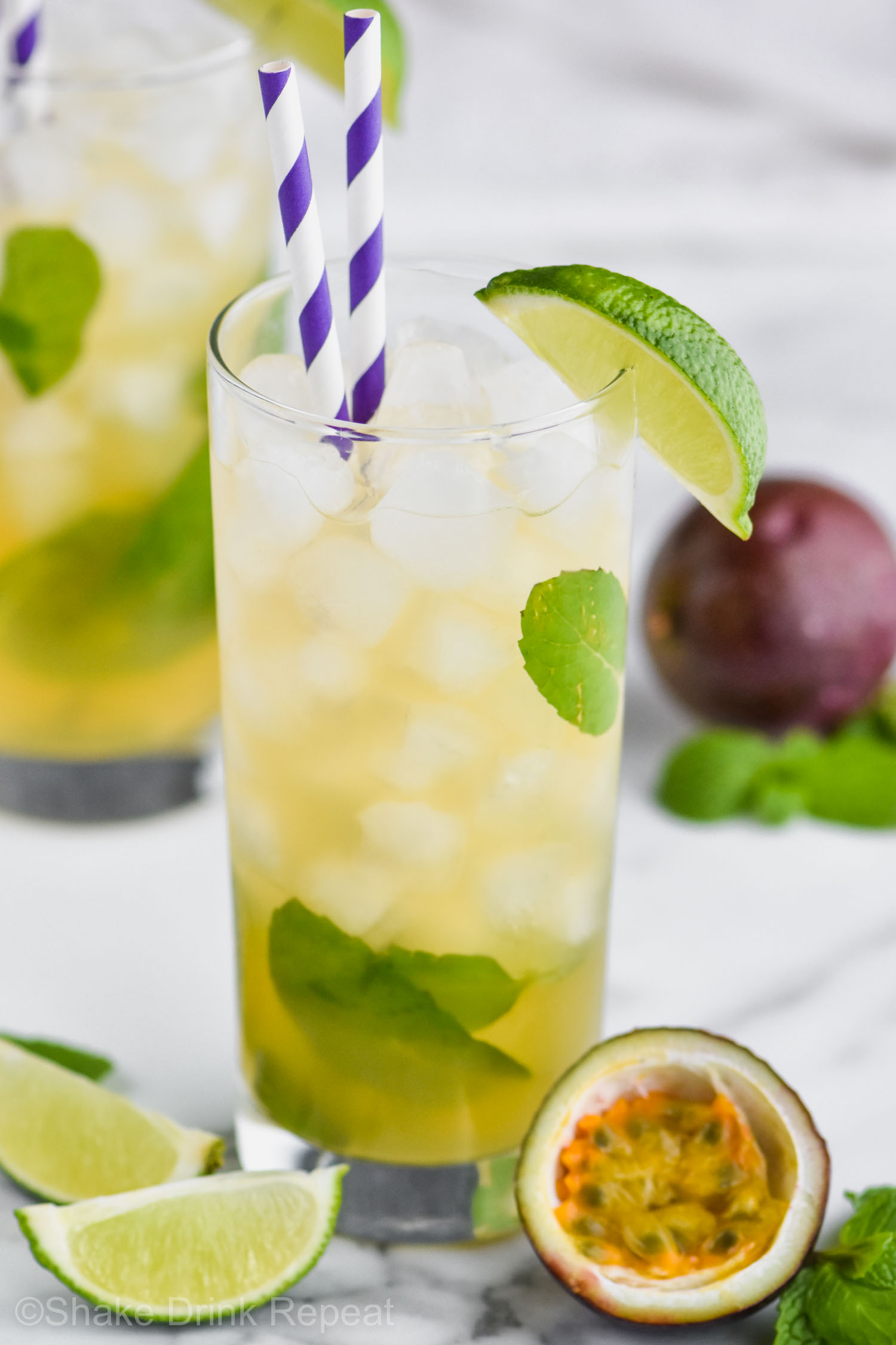 Two glasses of Passion Fruit Mojito with ice, straws, limes, mint and fresh fruit.