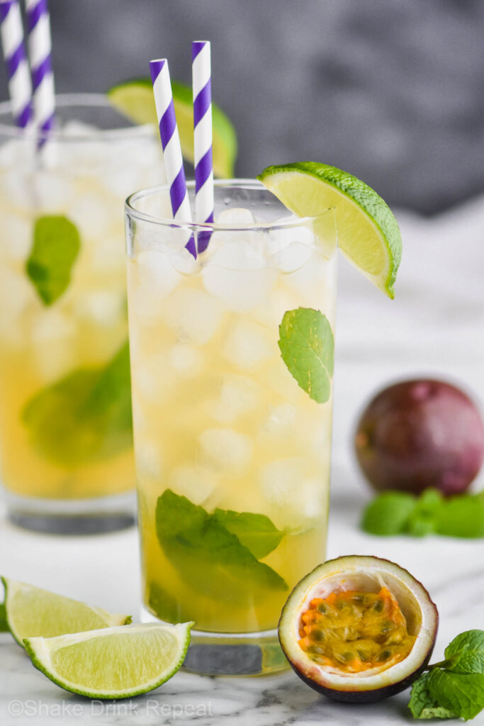 Two glasses of Passion Fruit Mojito with ice, straws, limes, mint and fresh fruit.