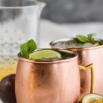 two copper mugs of passion fruit moscow mules with ice, limes, and fresh mint leaves