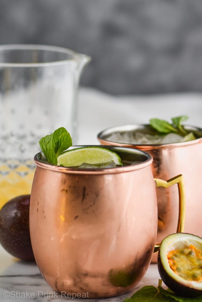 two copper mugs of passion fruit moscow mules with ice, limes, and fresh mint leaves