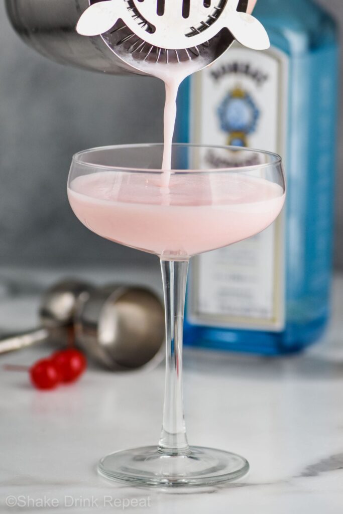 Shaker pouring pink lady into a glass