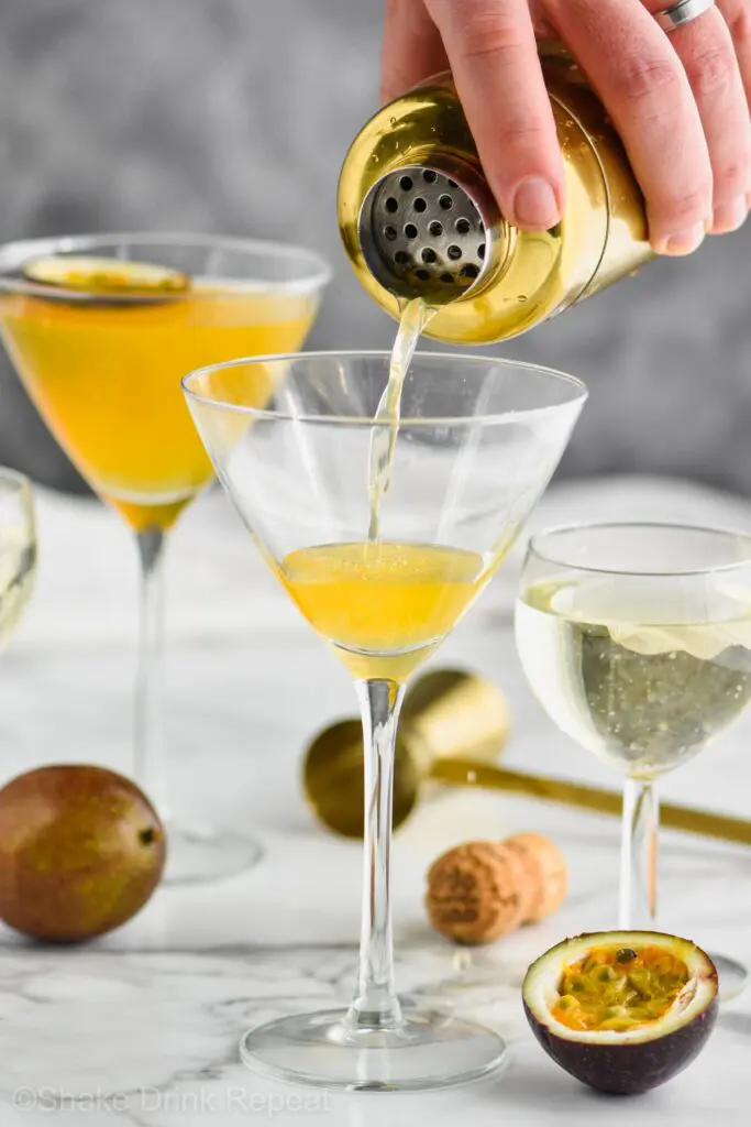 Glass with drink being poured into it with passion fruit garnishment around it