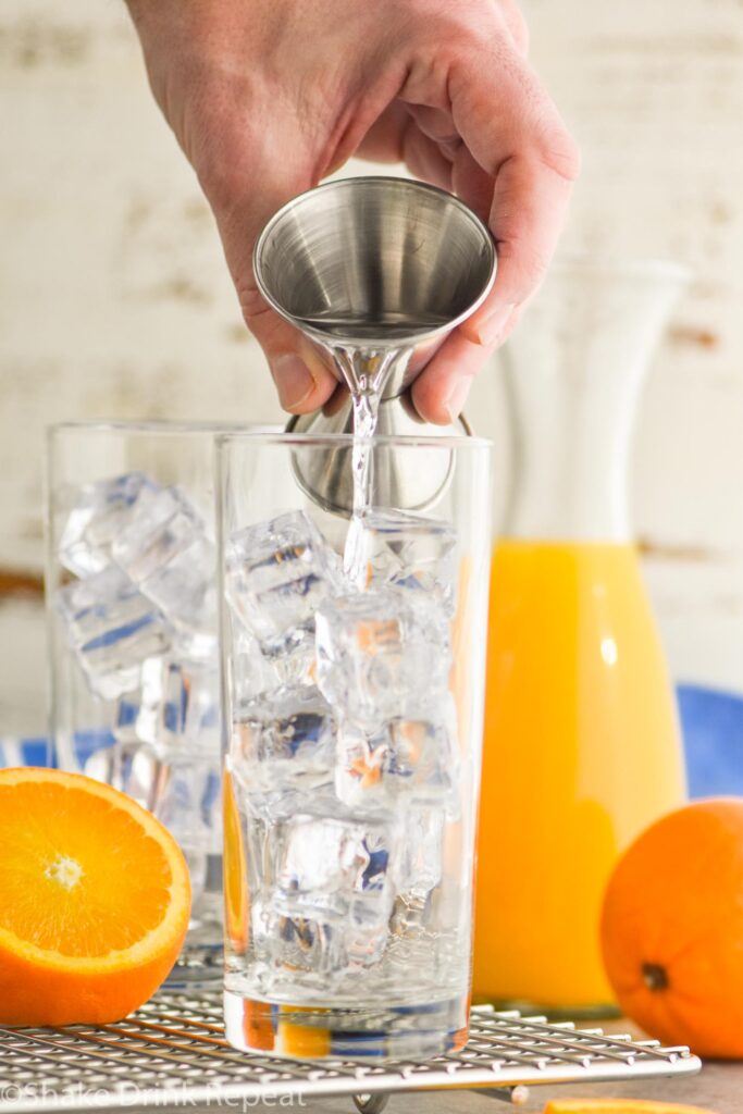 Glass filled with ice being filled with vodka, garnished with an orange