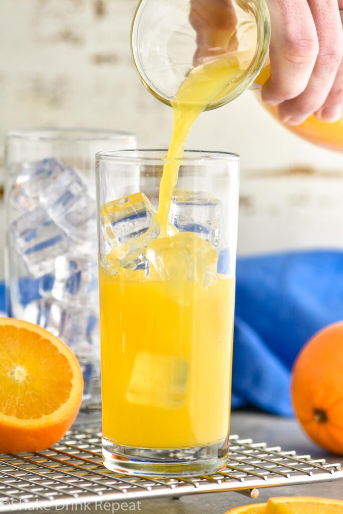 Glass being filled with Screwdriver cocktail, garnished with an orange