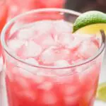 Picture of Sea Breeze being poured into a glass from a pitcher. Drink in a glass garnished with limes