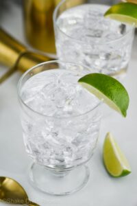 Two glasses of Vodka Press with ice, lime wedges, jigger and spoon off to the side