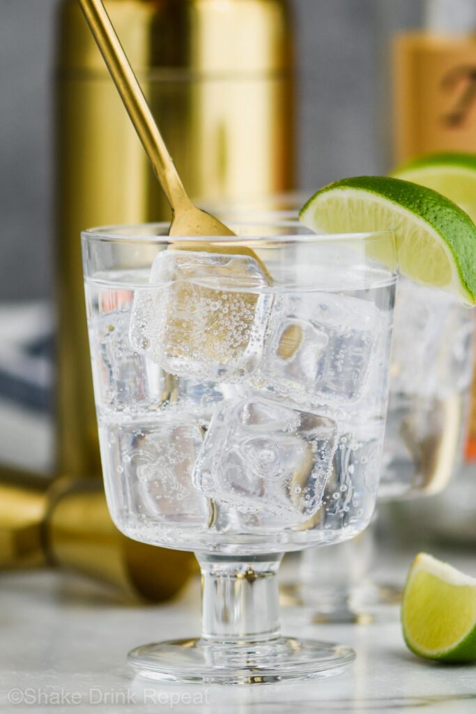 Glass of Vodka press with ice and lime wedge being stirred with spoon