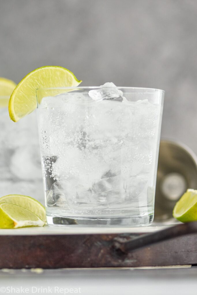 A glass of Vodka Soda with ice and lime wedges