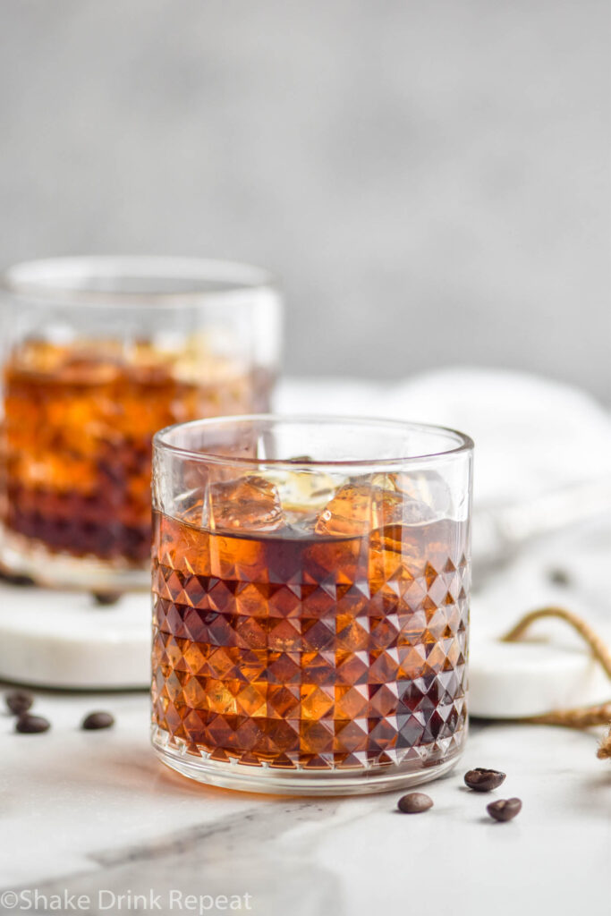 Two glasses of Black Russian with ice, surrounded by coffee beans