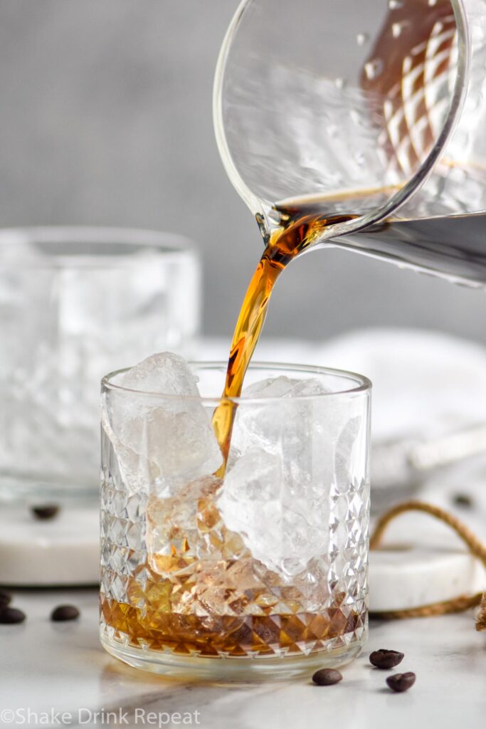 Pouring Black Russian into a glass with ice surrounded by coffee beans