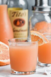 Two Glasses of Greyhound Cocktail with grapefruit wedge and ice and bottle of vodka and shaker in background