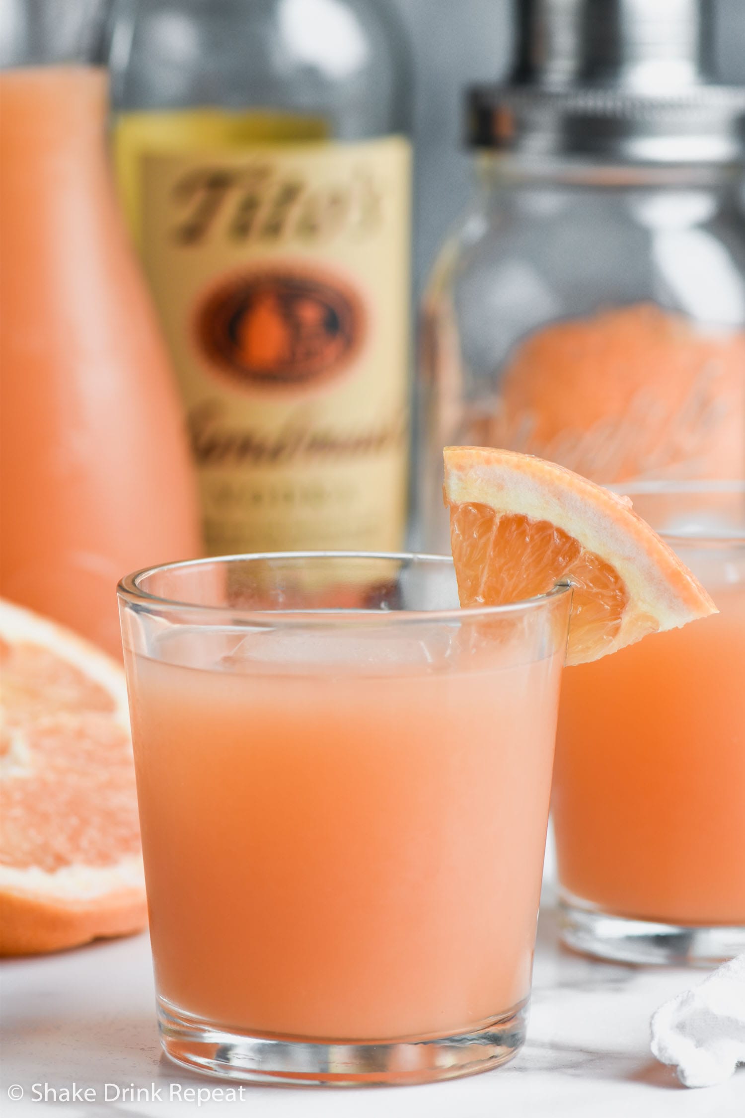 Two Glasses of Greyhound Cocktail with grapefruit wedge and ice and bottle of vodka and shaker in background