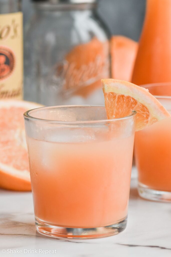 Glass of Greyhound Cocktail with grapefruit wedge and ice and bottle of vodka and shaker in background