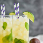 Two glasses of Passion Fruit Mojito with ice, straws, limes, mint and fresh fruit.