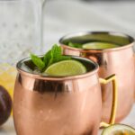 two copper mugs of passion fruit moscow mule with ice, lime, and fresh mint leaves