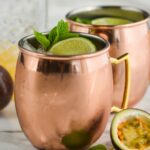 two copper mugs of passion fruit moscow mule with ice, lime, and fresh mint leaves