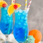 two glasses of Blue Lagoon cocktail recipe wtih orange slice garnish and cherry