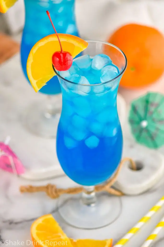 glass of blue lagoon cocktail with orange slice and cherry garnish