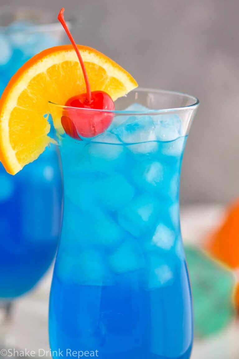 glass of Blue Lagoon cocktail with orange slice and cherry garnish