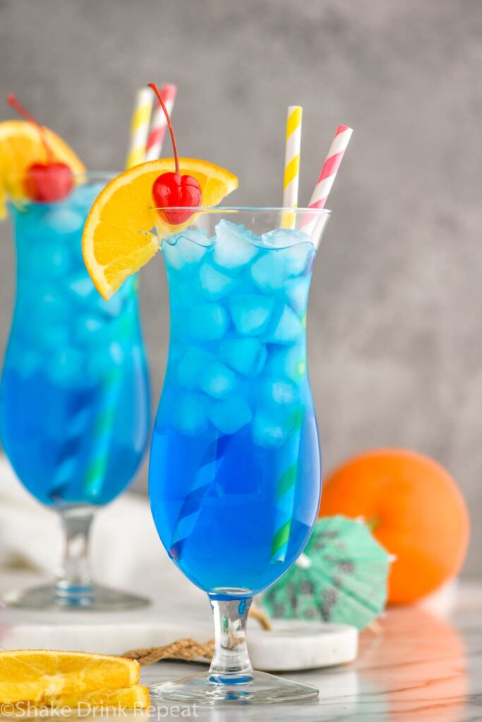 two glasses of Blue Lagoon cocktail recipe wtih orange slice garnish and cherry