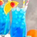 two glasses of Blue Lagoon cocktail with straws, orange slice, and cherry garnish