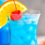 Glass of blue lagoon cocktail with orange slice and cherry garnish
