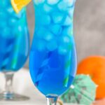 two glasses of Blue Lagoon cocktail with straws, orange slice and cherry garnish