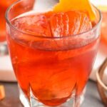 glass of boulevardier cocktail with ice and orange garnish