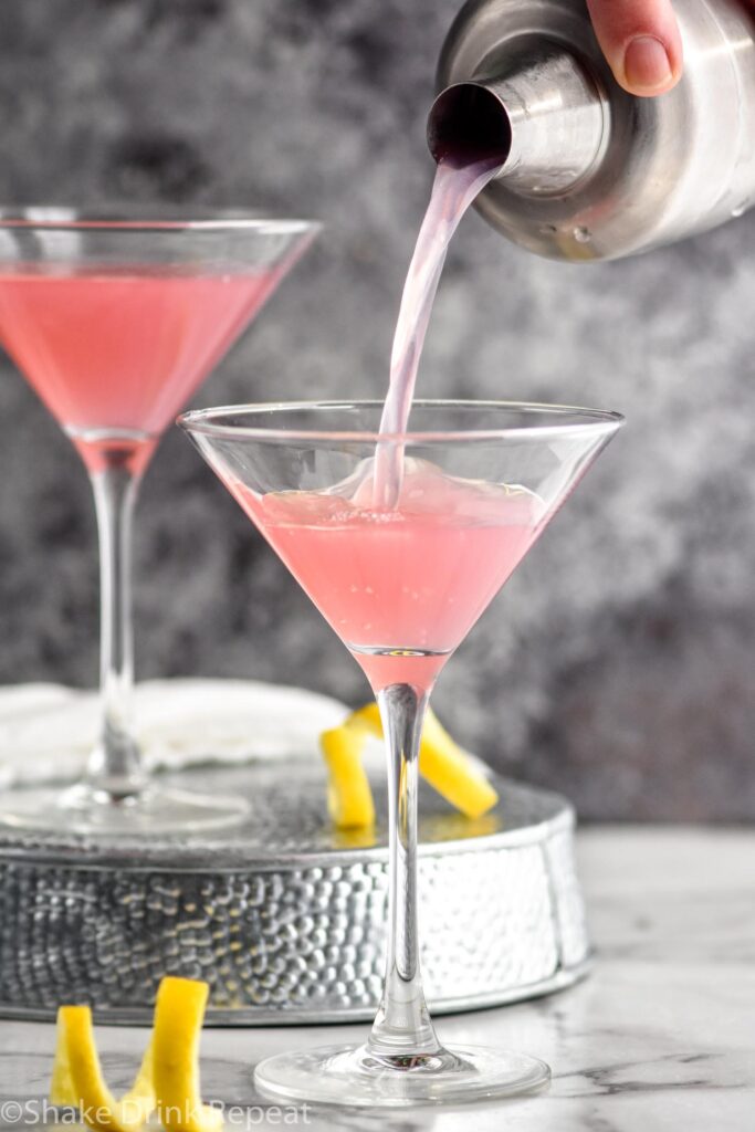 Cosmopolitan Cocktail being poured intoa glass garnished with a lemon twist