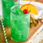 Two glasses of Drunk Leprechaun with orange and cherry garnish, spoon and straw on the side