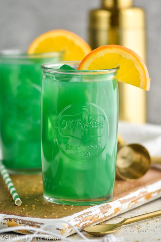 Two glasses of Drunk Leprechaun with orange garnish, spoon and straw on the side