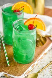 Two glasses of Drunk Leprechaun with orange and cherry garnish, spoon and straw on the side