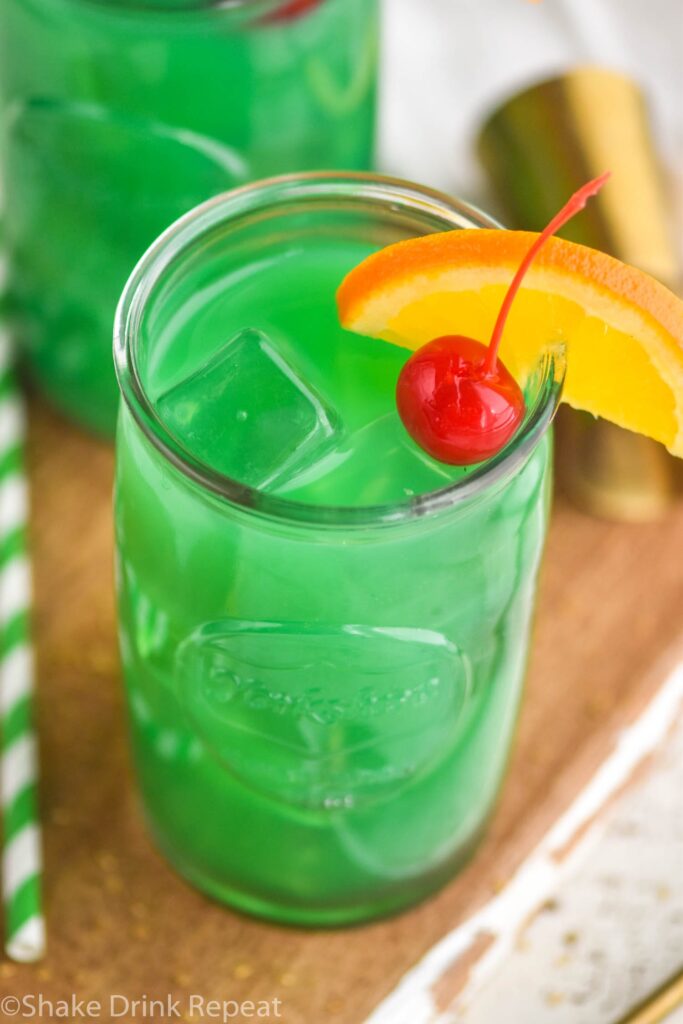 Two glasses of Drunk Leprechaun with orange and cherry garnish, spoon and straw on the side