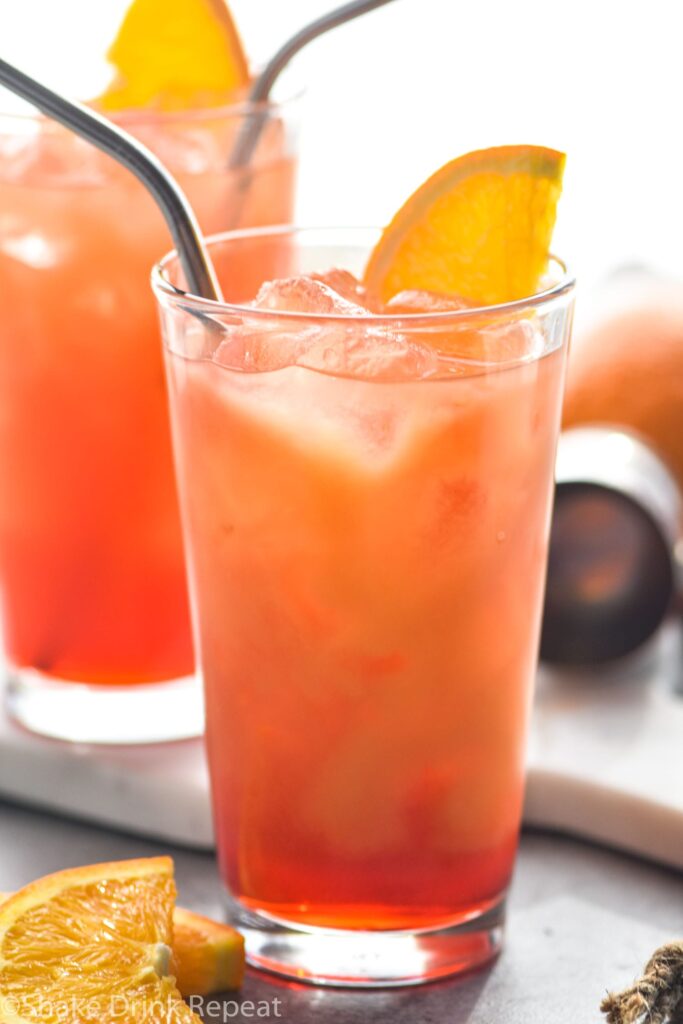two glasses of Garibaldi cocktails with ice, straws and orange garnish